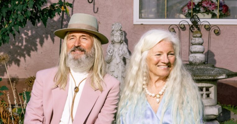 An older couple smiling together outside a pink house, aging gracefully