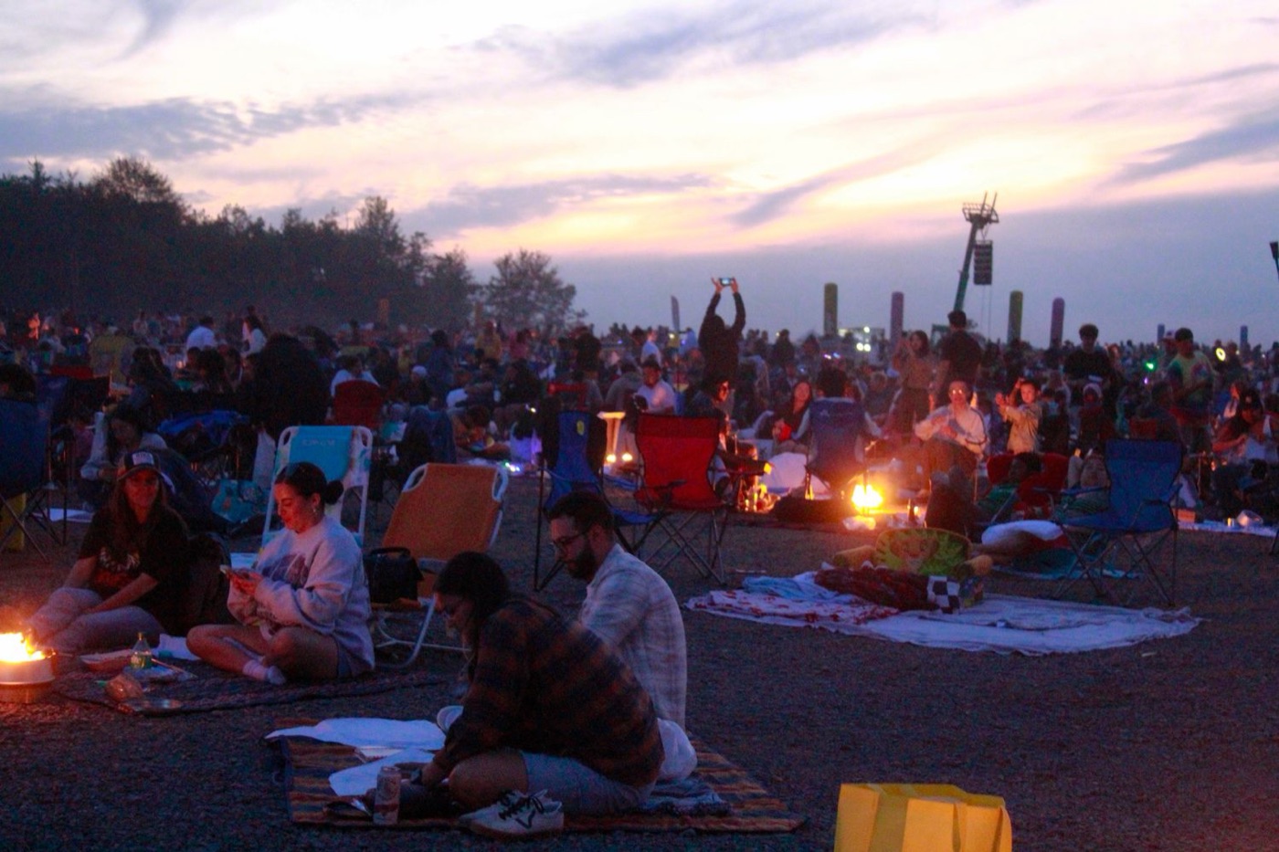 festival campground dusk - Blog Festival campground at dusk with people gathered around small fires under a purple sky