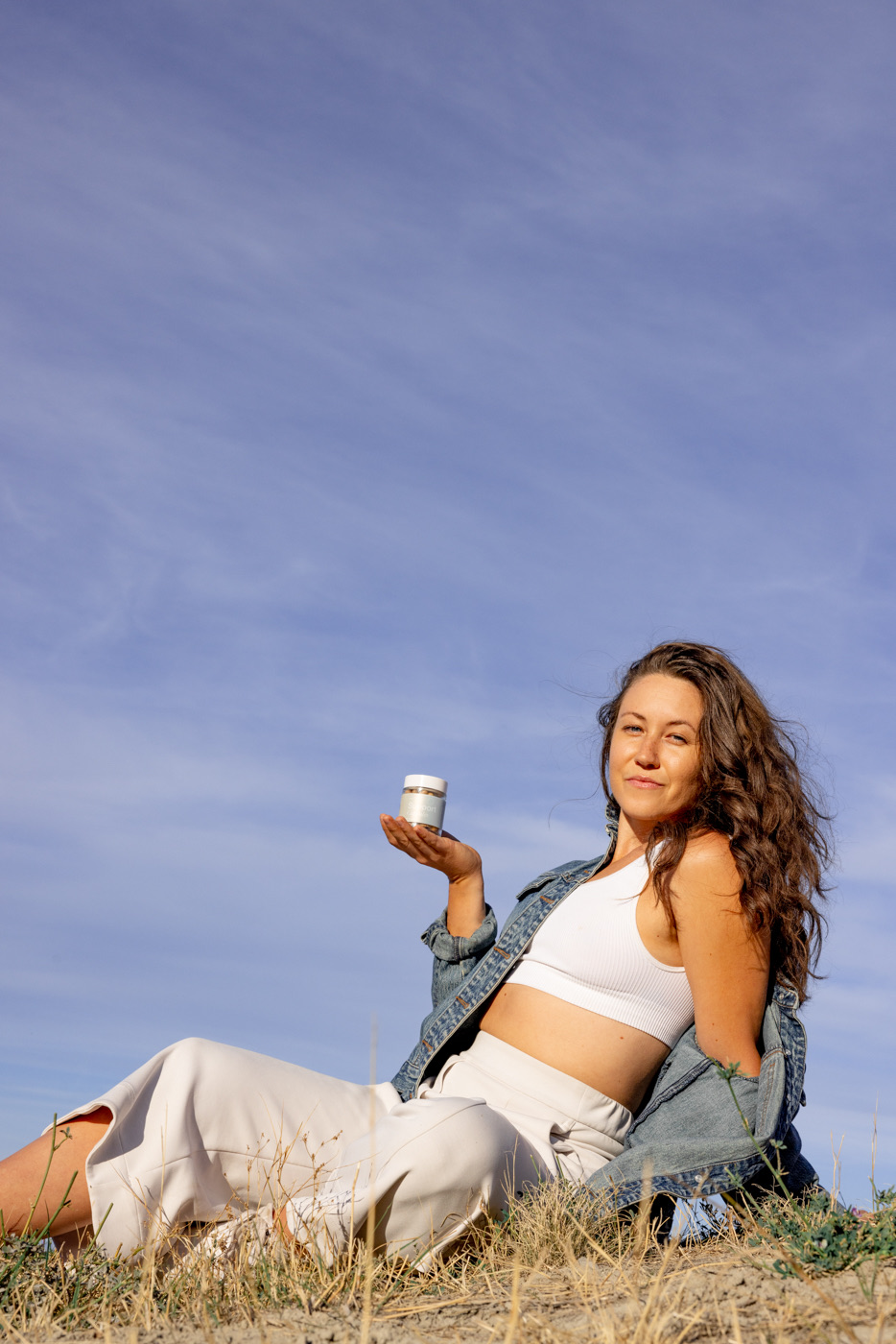 fall hillside walk support - Blog A woman in a denim jacket sitting on a golden hillside under a wide blue sky