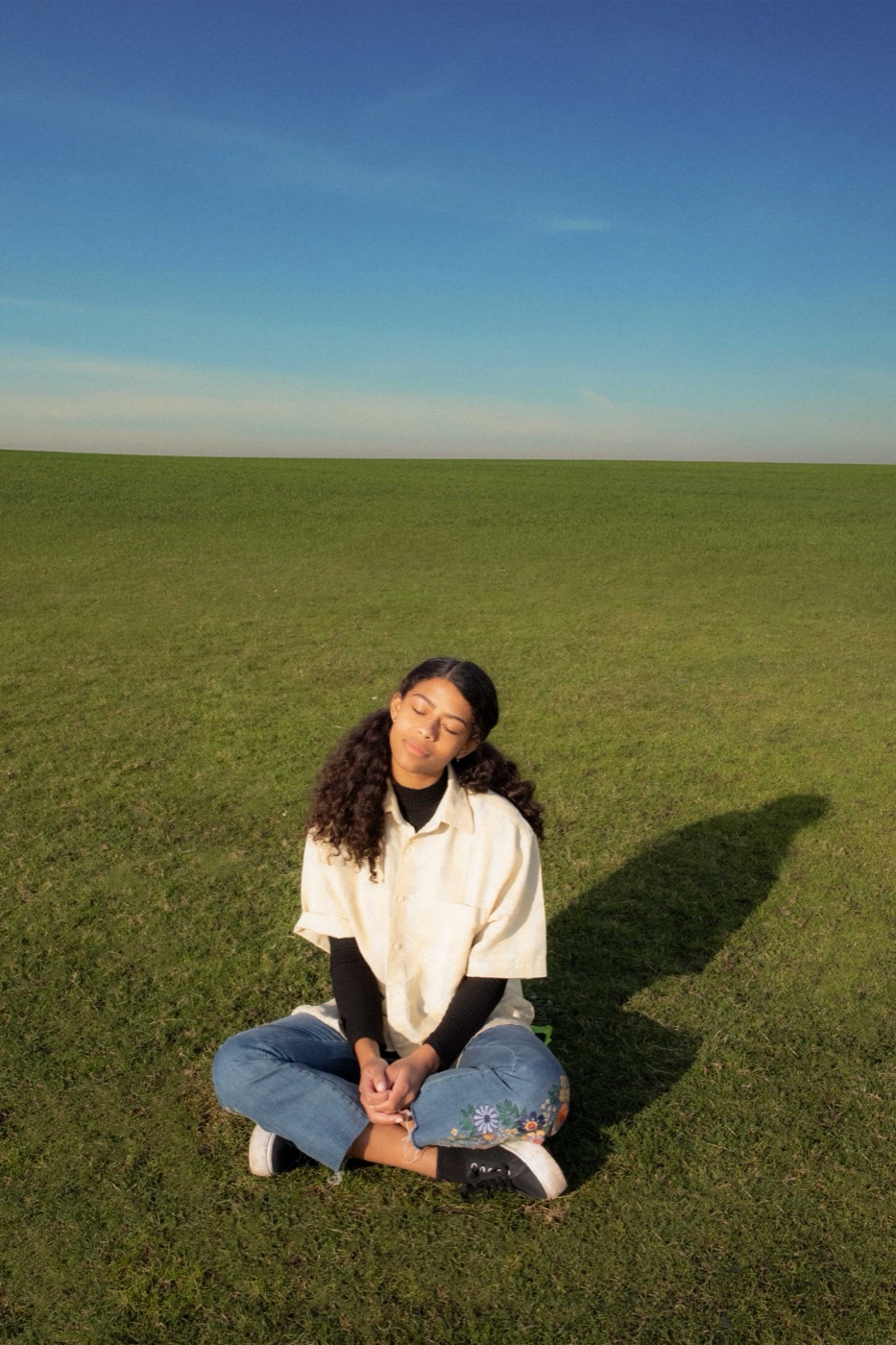 women microdosing calm - Blog A woman sitting cross legged in a green field on a clear day