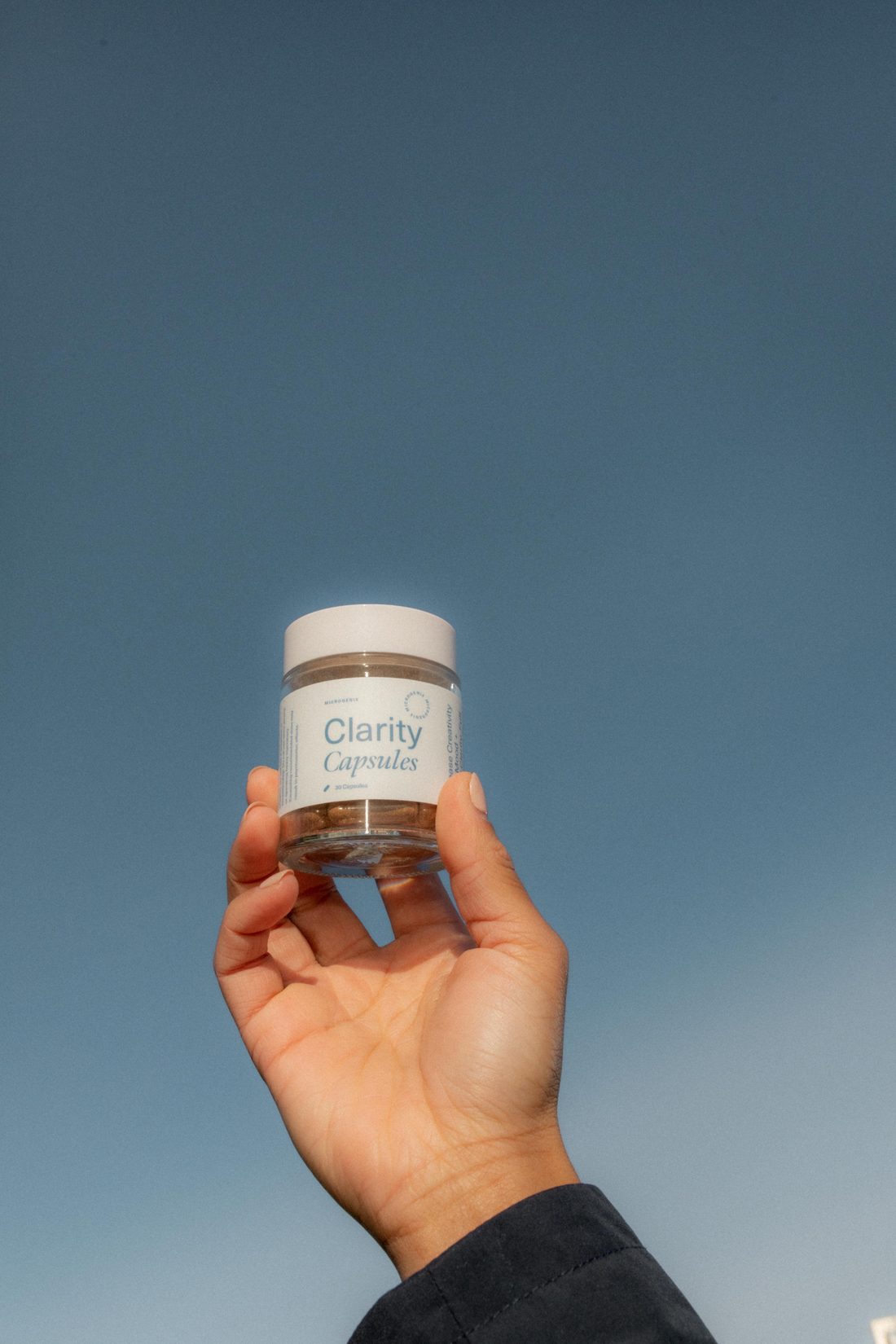 fall reset your space - Blog A hand holding a jar of Microgenix Clarity capsules against a clear blue sky