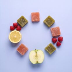 Sugared Magic Gummies cubes laid in a line between fresh fruit on a periwinkle surface