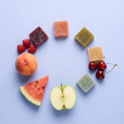 The five Magic Gummies flavors laid in a ring with fresh peach, cherries, watermelon, apple and raspberries