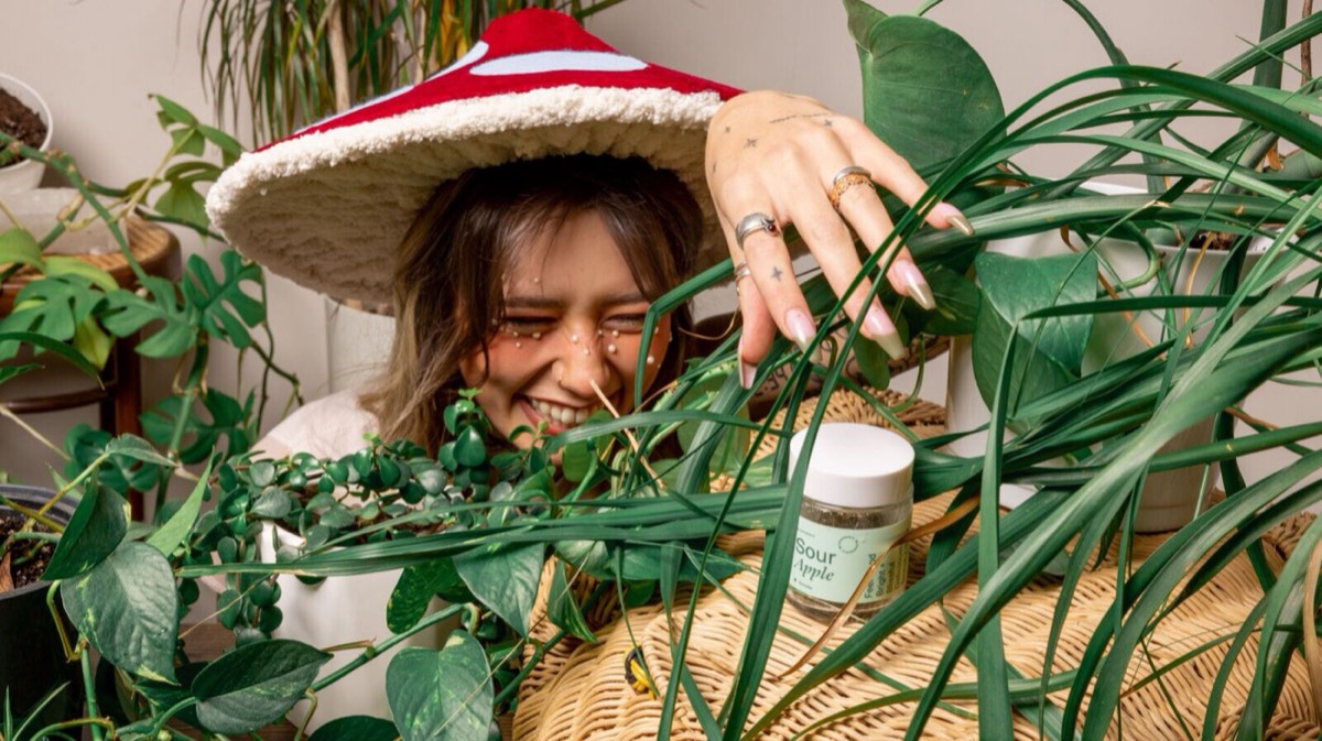 hw26 blog mgx hw hat laugh - Blog A woman in a mushroom hat laughing behind a jar of Microgenix capsules